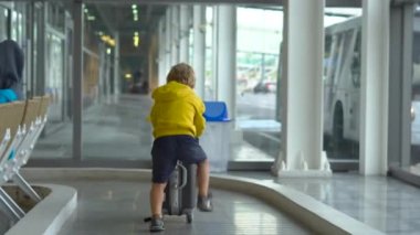 Little boy in a medical face mask playing with a suitcase in an airport