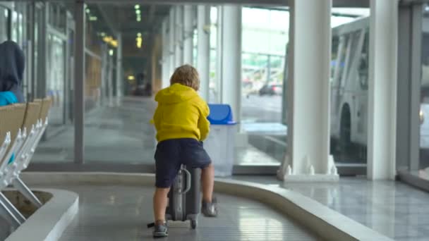 Kleiner Junge mit medizinischer Gesichtsmaske spielt auf einem Flughafen mit einem Koffer — Stockvideo