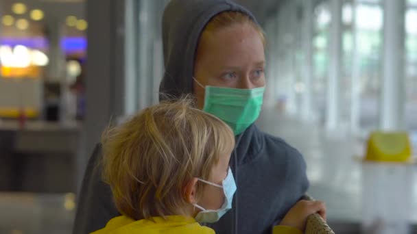 Menino e sua mãe em uma máscara médica em um aeroporto à espera de seu voo — Vídeo de Stock