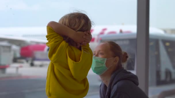 Liten pojke och hans mor i en medicinsk ansiktsmasker i en flygplats väntar på sin flygning — Stockvideo