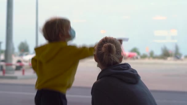 Kleiner Junge und seine Mutter mit medizinischer Gesichtsmaske auf einem Flughafen, der auf ihren Flug wartet — Stockvideo