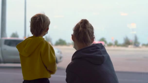 Мальчик и его мать в медицинских масках в аэропорту ждут своего рейса — стоковое видео