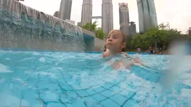 Slowmotion shot van een jongetje met plezier in een zwembad in een park — Stockvideo