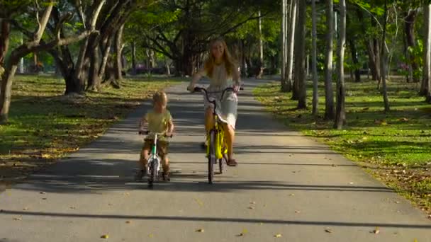 Steadycam schot van een jonge vrouw en haar zoontje rijden een fiets- en runbike in een tropisch park — Stockvideo