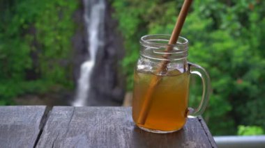 Bir kanyon ve şelale üzerinde destansı bir görünümü ile güzel bir kafede genç bir kadının slowmotion çekim buz ile çay içecekler. Travell bali kavramı