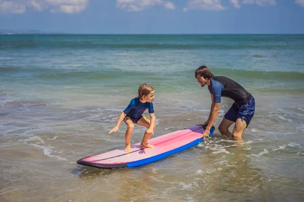 Padre o istruttore che insegna a suo figlio di 5 anni come navigare in mare in vacanza o in vacanza. Viaggio e sport con bambini concetto. Lezione di surf per bambini — Foto Stock