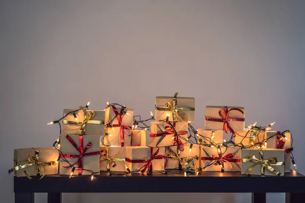 Sok ajándékot egy fekete fából készült asztal minden ünnep. Jelenleg csomagolva kézműves papírt egy piros és arany szalagot karácsonyra, születésnapjára, anyák nap vagy Valentin — Stock Fotó