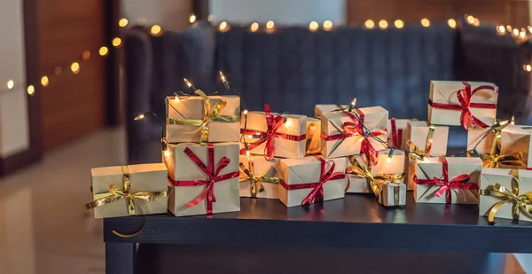 Πολλά δώρα σε ένα μαύρο ξύλινο τραπέζι για κάθε αργία. Παρόν τυλιγμένο σε χαρτί χειροτεχνίας με μια κόκκινη και χρυσή κορδέλα για τα Χριστούγεννα, γενέθλια, ημέρα της μητέρας ή του Αγίου Βαλεντίνου — Φωτογραφία Αρχείου