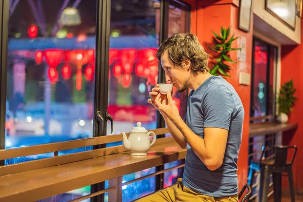 Молодой человек пьет китайский чай на фоне красных китайских фонарей в честь китайского Нового года — стоковое фото
