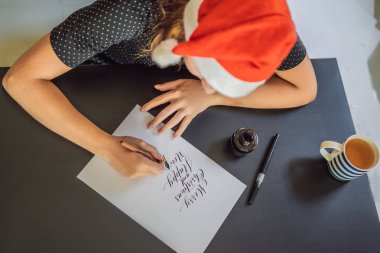 Mutlu noeller ve mutlu bir yeni yıl. Hattat Genç Kadın beyaz kağıda cümle yazıyor. Süs süslemeli harfler. Kaligrafi, grafik tasarım, yazı, el yazısı, oluşturma