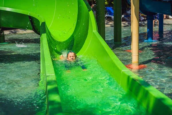 Glücklicher Junge auf der Wasserrutsche in einem Schwimmbad, der während der Sommerferien in einem wunderschönen tropischen Resort Spaß hat — Stockfoto