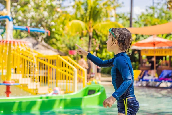 Niño feliz en el tobogán acuático en una piscina que se divierte durante las vacaciones de verano en un hermoso complejo tropical — Foto de Stock