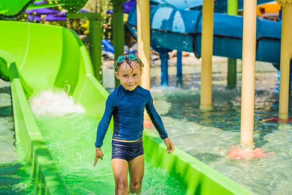 Niño feliz en el tobogán acuático en una piscina que se divierte durante las vacaciones de verano en un hermoso complejo tropical —  Fotos de Stock