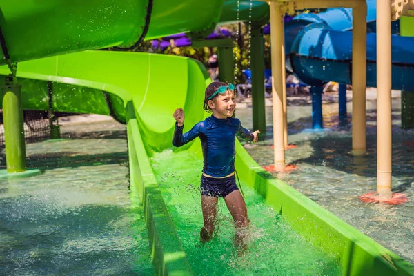 Счастливый мальчик на водной горке в бассейне развлекается во время летних каникул на красивом курорте — стоковое фото