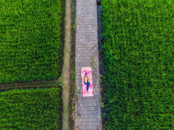Junge Frau praktiziert Yoga im Freien in Reisfeldern am Morgen während Wellness-Retreat in Bali. Blick aus der Drohne — Stockfoto