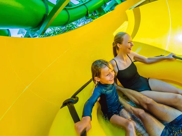 Mamá, papá e hijo en el parque acuático comiendo junto a la montaña rusa — Foto de Stock