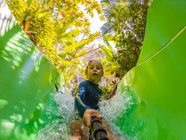 Joyeux garçon sur toboggan aquatique dans une piscine s'amuser pendant les vacances d'été dans une belle station tropicale — Photo