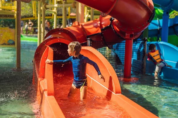 Menino feliz no slide de água em uma piscina se divertindo durante as férias de verão em um belo resort tropical — Fotografia de Stock