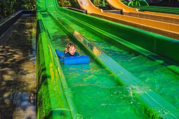 Niño feliz en el tobogán acuático en una piscina que se divierte durante las vacaciones de verano en un hermoso complejo tropical — Foto de Stock