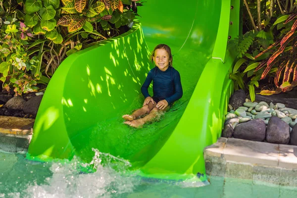 Niño feliz en el tobogán acuático en una piscina que se divierte durante las vacaciones de verano en un hermoso complejo tropical — Foto de Stock