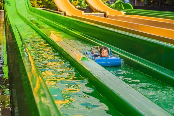 Niño feliz en el tobogán acuático en una piscina que se divierte durante las vacaciones de verano en un hermoso complejo tropical — Foto de Stock