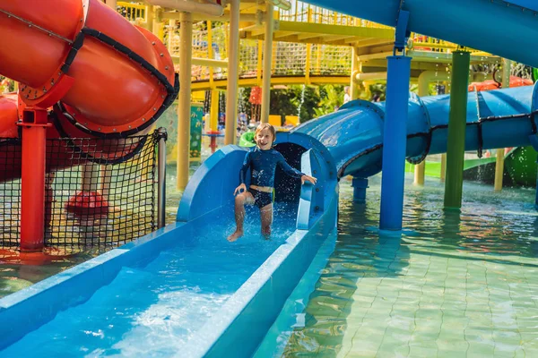 Glücklicher Junge auf der Wasserrutsche in einem Schwimmbad, der während der Sommerferien in einem wunderschönen tropischen Resort Spaß hat — Stockfoto