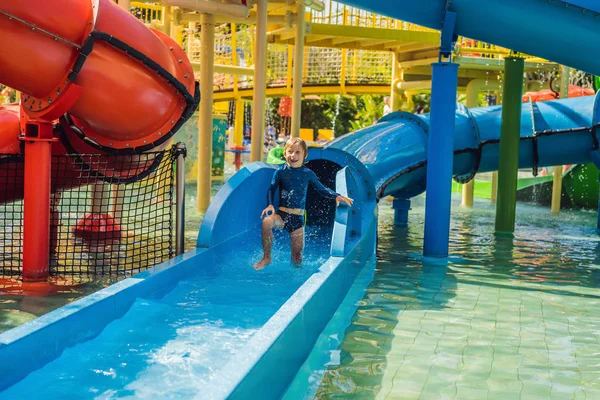 Menino feliz no slide de água em uma piscina se divertindo durante as férias de verão em um belo resort tropical — Fotografia de Stock