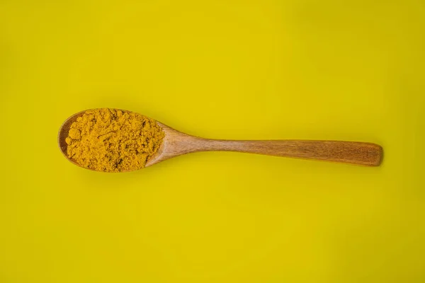 Polvo de cúrcuma en una cuchara de madera sobre un fondo amarillo — Foto de Stock