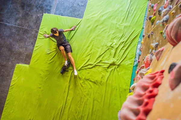 Hombre musculoso practicando escalada en roca en una pared de roca en el interior — Foto de Stock