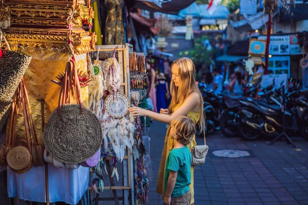 Mamá e hijo viajeros eligen recuerdos en el mercado en Ubud en Bali, Indonesia — Foto de Stock