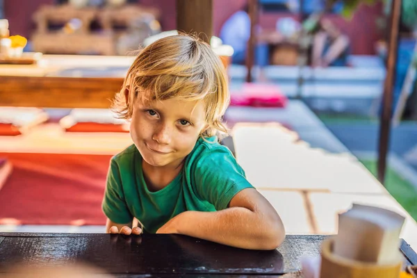 Rapaz emocional numa mesa num café. Bonito menino sentado no restaurante ao ar livre no dia de verão. criança em um café à espera de sua ordem — Fotografia de Stock