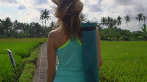 Slowmotion steadicam toma de una mujer joven con matemáticas de yoga caminando a través de un hermoso campo de arroz — Vídeo de stock