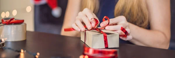 若い女性がプレゼントを梱包しています。クリスマスや新年のための赤と金のリボンでクラフトペーパーに包まれたプレゼント。女性は彼女の子供のバナー、ロングフォーマットのためのアドベントカレンダーを作ります — ストック写真