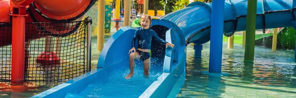 Niño feliz en el tobogán acuático en una piscina que se divierte durante las vacaciones de verano en un hermoso complejo tropical BANNER, FORMATO LARGO — Foto de Stock