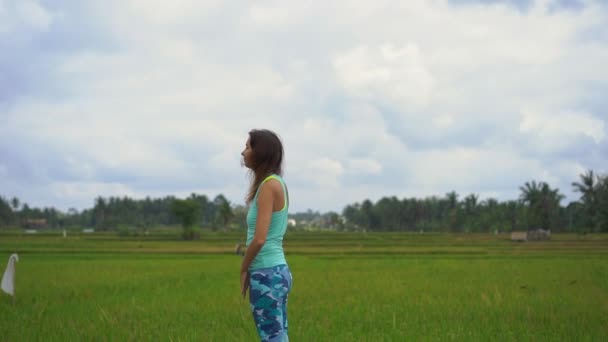 Αργή βολή μιας νεαρής γυναίκας που εξασκείτε γιόγκα σε ένα όμορφο χωράφι ρυζιού — Αρχείο Βίντεο
