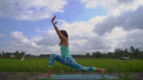 Slowmotion Steadicam skott av en ung kvinna som tränar yoga på ett vackert risfält — Stockvideo