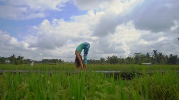 Slowmotion steadicam shot d'une jeune femme pratiquant le yoga sur un beau champ de riz — Video