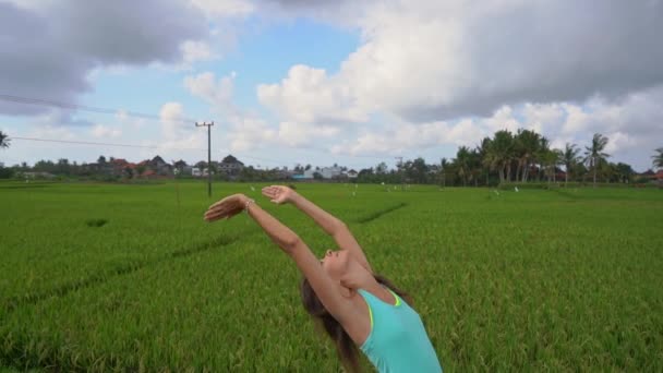 Slowmotion steadicam tiro de uma jovem mulher com ioga matemática andando através de um belo campo de arroz — Vídeo de Stock