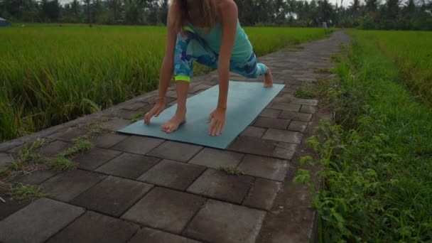 Slowmotion steadicam shot of a young woman with yoga math walking through a beautiful rice field — Stock Video