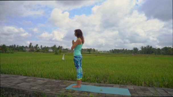 Αργή βολή μιας νεαρής γυναίκας που εξασκείτε γιόγκα σε ένα όμορφο χωράφι ρυζιού — Αρχείο Βίντεο