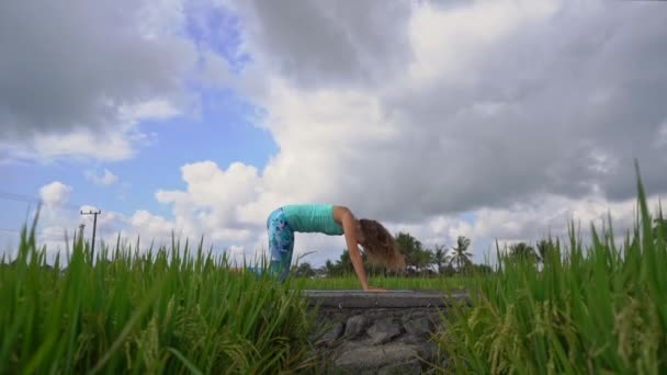 Slowmotion steadicam tiro de uma jovem mulher com ioga matemática andando através de um belo campo de arroz — Vídeo de Stock