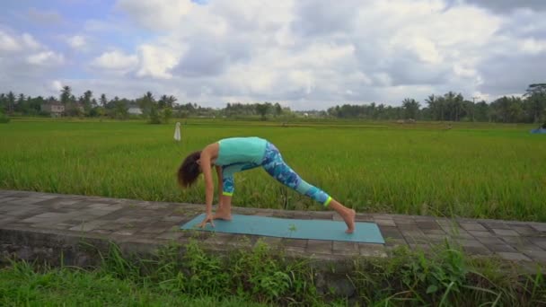 Slowmotion skott av en ung kvinna som tränar yoga på ett vackert risfält — Stockvideo