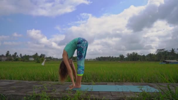 Смугастий постріл уповільнення молодої жінки, що практикує йогу на красивому рисовому полі — стокове відео