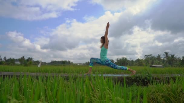 Slowmotion Steadicam skott av en ung kvinna som tränar yoga på ett vackert risfält — Stockvideo