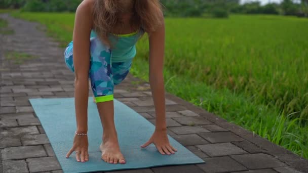 Slowmotion skott av en ung kvinna som tränar yoga på ett vackert risfält — Stockvideo