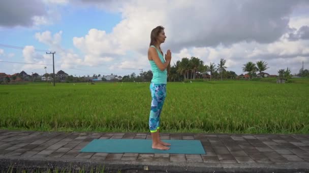 Slowmotion colpo steadicam di una giovane donna con matematica yoga a piedi attraverso una bella risaia — Video Stock