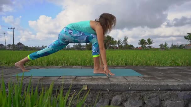 Slowmotion Steadicam skott av en ung kvinna med yoga matte gå igenom en vacker risfält — Stockvideo