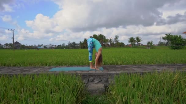 Slowmotion steadicam shot d'une jeune femme avec des mathématiques de yoga marchant à travers un beau champ de riz — Video