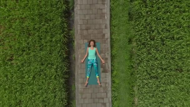 Luchtfoto van een jonge vrouw die liegen en mediteren op een pad door een prachtig rijstveld — Stockvideo
