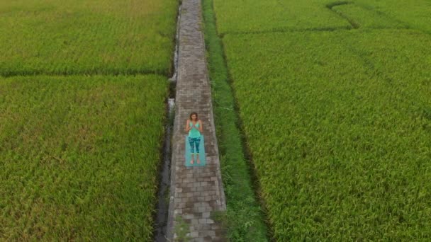 Εναέρια αργή βολή μιας νεαρής γυναίκας εξάσκηση γιόγκα σε ένα όμορφο χωράφι ρυζιού — Αρχείο Βίντεο